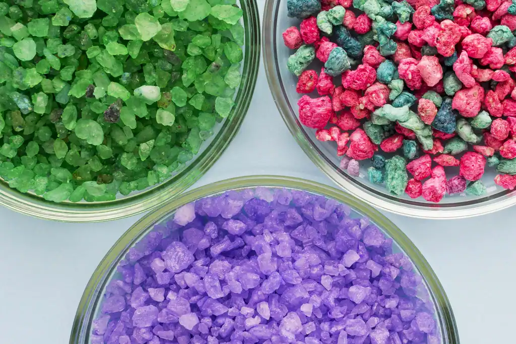 Grânulos plásticos em verde, vermelho e roxo, amostras de matéria-prima